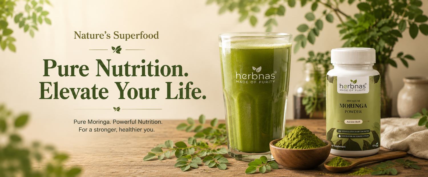 A glass of green smoothie and a bottle of herbnas Moringa Powder alongside bowls of green powder, set on a wooden table with decorative green leaves and herbs in a warm, natural setting.